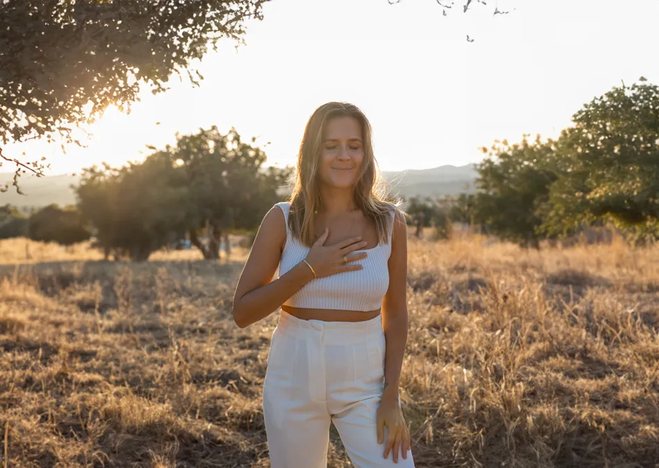 Corinna fässt sich ans Herz und posiert lächelnd in natürlicher Landschaft